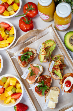 Canapes, fingerfood, orange juice, tomatoes and fruit bowls placed on top of a table. 