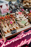 Fein drapierte Canapés und Bruschetta auf einem Catering-Tisch mit Beschriftungsschildern, präsentiert vor einem leuchtenden 'Charcuterie Düsseldorf'-Neonschild, das ein elegantes und ansprechendes Ambiente für Veranstaltungen bietet.