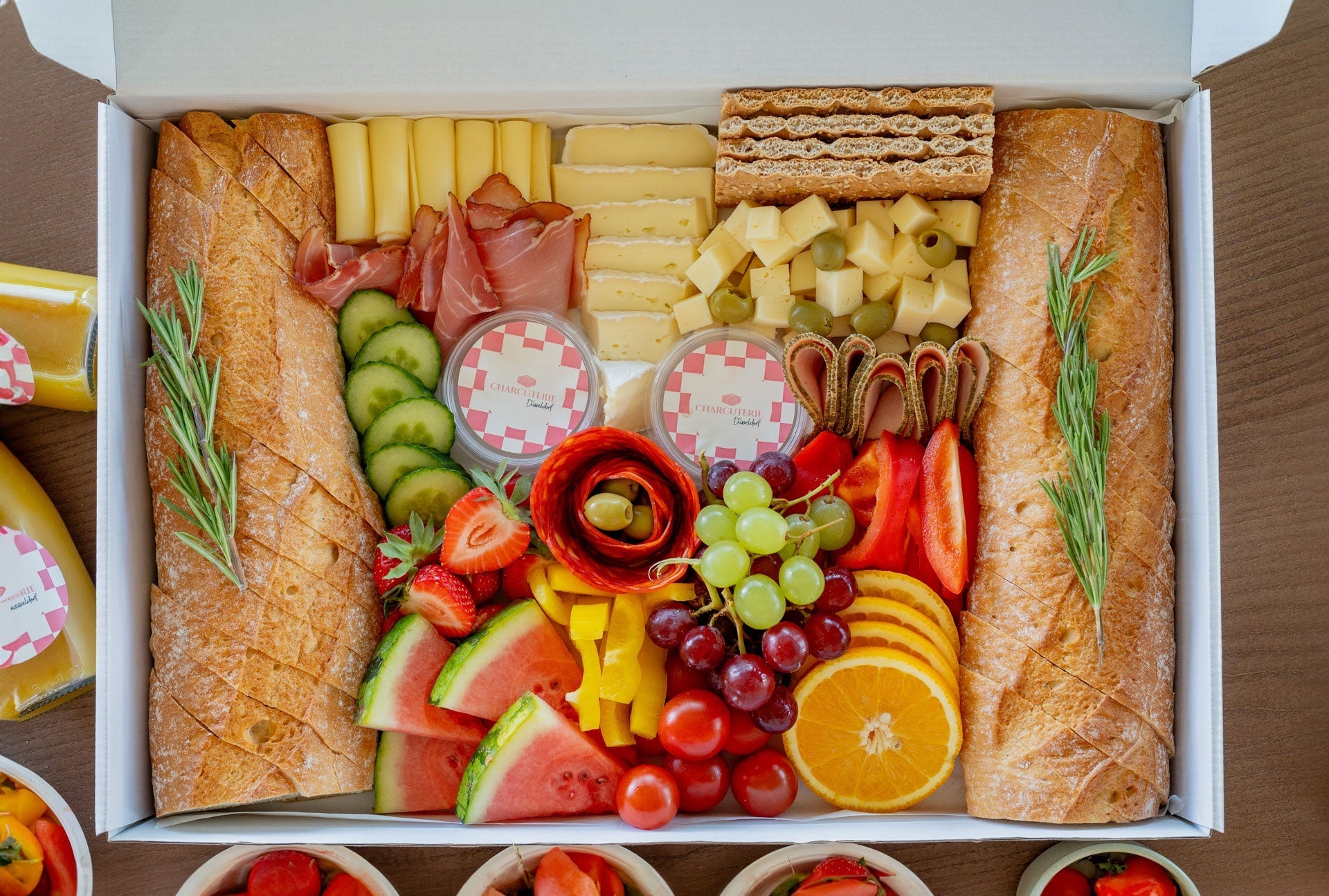 Charcuterie Box including baguette, cheese, sausages, fruits, veggies, dips and jam. Decorated beautifully in a catering box. 