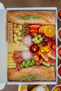 Charcuterie Box including baguette, cheese, sausages, fruits, veggies, dips and jam. Decorated beautifully in a catering box. 