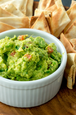 Guacamole Dip with crackers in the background. Made of avocado, bell peppers and more. 