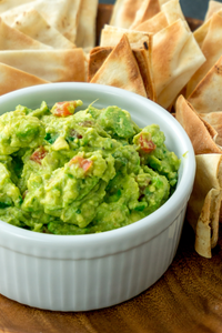Guacamole Dip with crackers in the background. Made of avocado, bell peppers and more. 