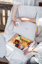 Cargar imagen en el visor de la galería, A picture of an elegantly dressed person holding a &#39;I ♥ MUM&#39; cookie over a beautifully arranged box filled with a luxurious selection of picnic foods, including various cheeses, fruits, and bread. The image conveys a sense of preparation for a sophisticated Mother&#39;s Day celebration or a special occasion picnic, emphasizing thoughtfulness and care in the presentation.
